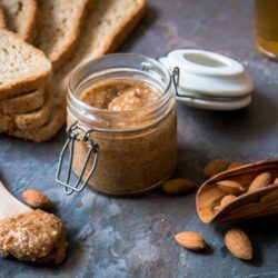 Tarrina de Amlou con almendras crudas sobre piedra de pizarra, junto con miel y aceite de argán