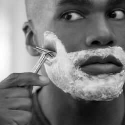 Chico de color afeitandose frente al espejo en blanco y negro