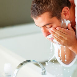 Persona limpiando la cara después del afeitado. Tiene restos de espuma por la cara.