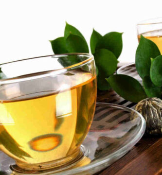 Te verde con taza transparrente encima de mesa de madera.